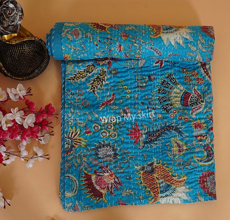 May include: A turquoise blue kantha quilt with a floral and paisley pattern. The quilt is hand-stitched and has a soft, textured surface.