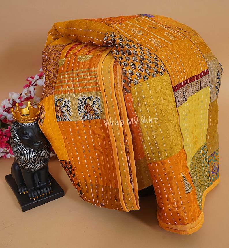 Puede incluir: Una colcha kantha amarilla y dorada hecha de saris reciclados. La colcha est&aacute; compuesta por muchos cuadrados de tela diferentes, cada uno con un patr&oacute;n diferente. La colcha est&aacute; cosida a mano y tiene un aspecto r&uacute;stico y hermoso.