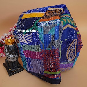 May include: A patchwork quilt with a variety of blue, green, yellow, and red fabrics. The quilt is stitched together with white thread. The text "Wrap My Skirt" is visible on the quilt. The quilt is folded and appears to be a blanket or throw.