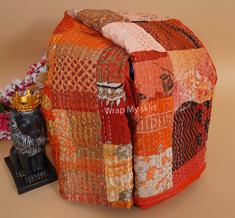 Puede incluir: Una colcha de retazos hecha de varias telas en tonos naranja, marr&oacute;n y blanco. La colcha est&aacute; doblada y tiene un dise&ntilde;o cosido. El texto "Wrap My Skirt" es visible en la colcha.