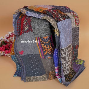 Könnte beinhalten: Eine mehrfarbige Patchworkdecke mit verschiedenen Mustern und Texturen. Die Decke besteht aus Stoffquadraten, die mit weißem Faden zusammengenäht sind. Der Text "Wrap My Skirt" ist auf der Decke zu sehen. Die Farben umfassen Grau, Rot, Blau und Orange.