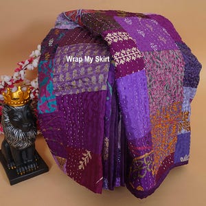 Könnte beinhalten: Eine gefaltete Patchwork-Steppdecke in Lilatönen mit verschiedenen Stoffmustern und Texturen. Die verschiedenen Abschnitte und Nähte der Steppdecke sind sichtbar. Der Text "Wrap My Skirt" ist zu sehen.
