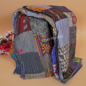 Pu&ograve; includere: Una trapunta patchwork realizzata con ritagli di stoffa colorati. La trapunta &egrave; piegata ed esposta su una superficie marrone chiaro. La trapunta presenta una variet&agrave; di motivi e colori, tra cui blu, verde, rosso, arancione e giallo. La trapunta &egrave; cucita con filo bianco. Il testo "Wrap Myskirt" &egrave; visibile sulla trapunta.