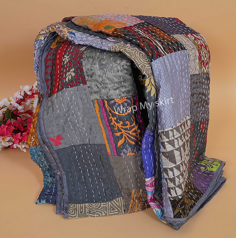Pu&ograve; includere: Una trapunta patchwork realizzata con ritagli di stoffa colorati. La trapunta &egrave; piegata ed esposta su una superficie marrone chiaro. La trapunta presenta una variet&agrave; di motivi e colori, tra cui blu, verde, rosso, arancione e giallo. La trapunta &egrave; cucita con filo bianco. Il testo "Wrap Myskirt" &egrave; visibile sulla trapunta.