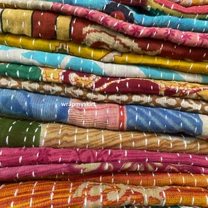Op de afbeelding: Een stapel kleurrijke kantha-dekens met ingewikkelde stiksels en patronen. De dekens zijn gemaakt van gerecyclede sari's en zijn een traditioneel Indiaas ambacht.