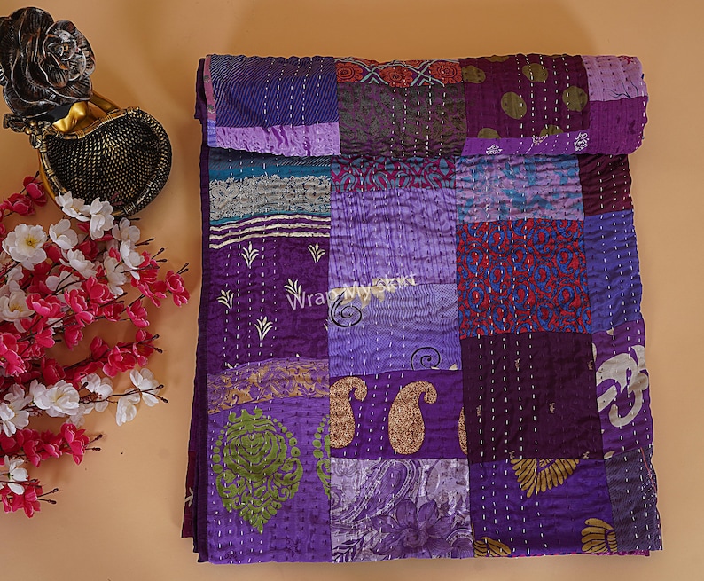 May include: Purple kantha quilt with a patchwork design. The quilt is made of various fabrics with different patterns and textures. The quilt is hand-stitched and has a unique, rustic look.