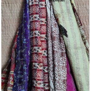 May include: A collection of five colourful kantha quilts, featuring a variety of floral and geometric patterns. The quilts are made from recycled saris and are hand-stitched with intricate details. The quilts are arranged in a vertical stack, with the top quilt being a light green colour and the bottom quilt being a deep purple colour.