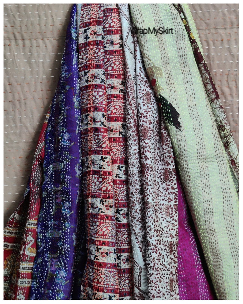 May include: A collection of five colourful kantha quilts, featuring a variety of floral and geometric patterns. The quilts are made from recycled saris and are hand-stitched with intricate details. The quilts are arranged in a vertical stack, with the top quilt being a light green colour and the bottom quilt being a deep purple colour.