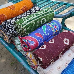 Könnte beinhalten: Ein Stapel bunter Kantha-Steppdecken, die auf einem Metallwagen aufgerollt sind. Die Decken sind aus Baumwolle und haben komplizierte Muster in Blautönen, Grün, Rot, Orange und Braun.