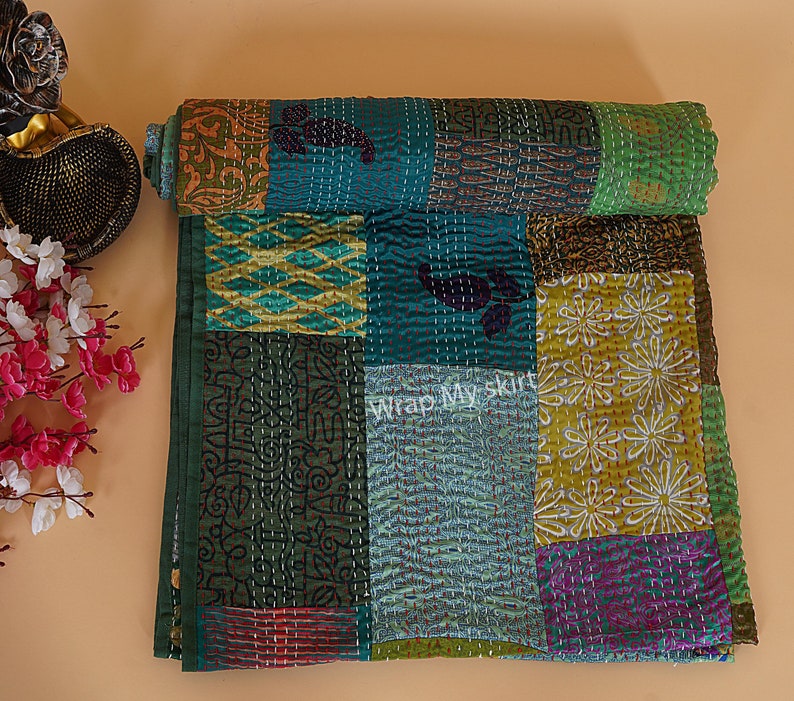May include: A patchwork quilt made of various fabrics in shades of green, blue, yellow, and purple. The quilt is hand-stitched and has a unique, rustic look. "Wrap My Skirt" is printed on the quilt.