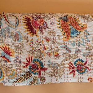 May include: A white kantha quilt with a floral pattern in shades of red, yellow, blue, and green. The quilt is made of cotton and has a hand-stitched design.