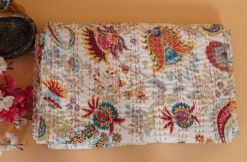 May include: A white kantha quilt with a floral pattern in shades of red, yellow, blue, and green. The quilt is made of cotton and has a hand-stitched design.