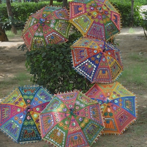 May include: A collection of colorful, decorative umbrellas with intricate embroidered patterns. The umbrellas feature a variety of colors, including pink, green, yellow, and blue, with elephant and floral designs. Each umbrella has a fringe trim.
