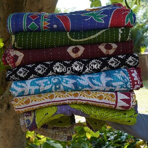 May include: A stack of eight colourful kantha quilts with various patterns and designs. The quilts are made of cotton and are hand-stitched. The quilts are folded and stacked on top of each other. The quilts are a variety of colours, including blue, green, red, brown, black, and white.