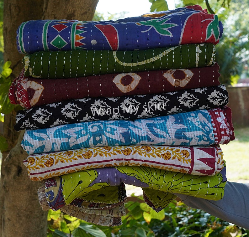 May include: A stack of eight colourful kantha quilts with various patterns and designs. The quilts are made of cotton and are hand-stitched. The quilts are folded and stacked on top of each other. The quilts are a variety of colours, including blue, green, red, brown, black, and white.