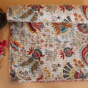May include: A white kantha quilt featuring a floral pattern in shades of red, yellow, blue, and green. The quilt is hand-stitched and displays a traditional Indian design.