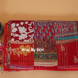 Könnte beinhalten: Ein Patchwork-Textil mit rotem Hintergrund und verschiedenen gemusterten Flicken in Weiß, Blau und Gelb. Der Text "Wrap My Skirt" ist sichtbar. Das Textil ist wahrscheinlich ein Quilt oder Dekorationsstoff.
