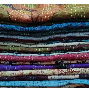 May include: A stack of colorful fabric squares with intricate stitching, likely for a quilt or patchwork project. The fabric is a mix of patterns and colors, including blue, green, red, and purple.