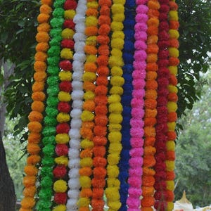 Puede incluir: Una vibrante guirnalda de flores de caléndula en varios colores, incluyendo naranja, amarillo, verde, blanco, azul, rosa y rojo. Las flores están ensartadas, creando una exhibición colorida y festiva, ideal para celebraciones y decoraciones.