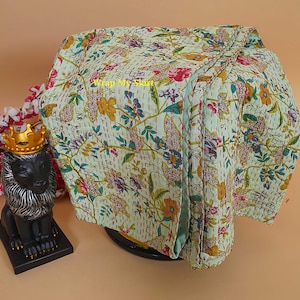 Peut inclure: Une courtepointe florale pliée, vert clair, avec une variété de fleurs et de feuilles colorées. La courtepointe a un motif cousu et le texte "Wrap My Skirt". Une statue de lion noir avec une couronne dorée est à gauche.