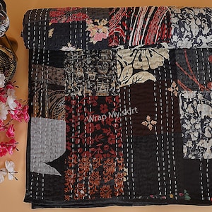 Puede incluir: Colcha kantha negra con un diseño de patchwork que presenta varios patrones florales y geométricos. La colcha está hecha de algodón y está cosida a mano. La colcha está enrollada en la esquina superior izquierda de la imagen. El texto "Wrap My Skirt" es visible en el centro de la colcha.