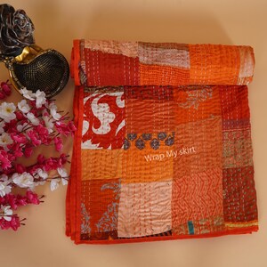 May include: A patchwork quilt made of various shades of orange and red fabric. The quilt is hand-stitched and has a unique, rustic look. The text "Wrap My skirt" is visible on the quilt.