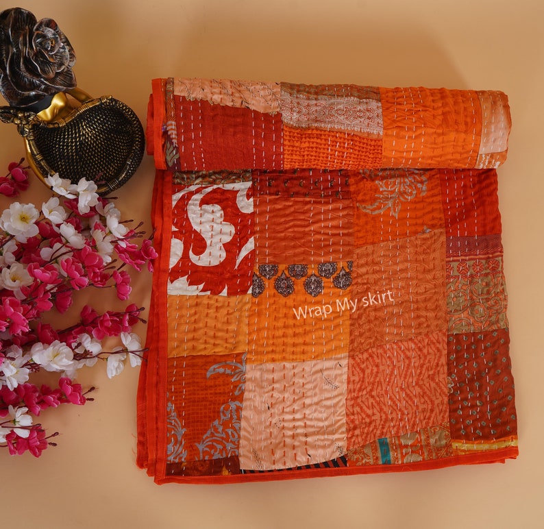 May include: A patchwork quilt made of various shades of orange and red fabric. The quilt is hand-stitched and has a unique, rustic look. The text "Wrap My skirt" is visible on the quilt.