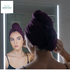 A woman wearing a mulberry coloured good wash day organic T-shirt hair towel whilst looking into a mirror.