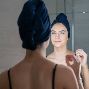 A woman wearing a navy blue good wash day organic T-shirt hair towel whilst looking into a mirror.