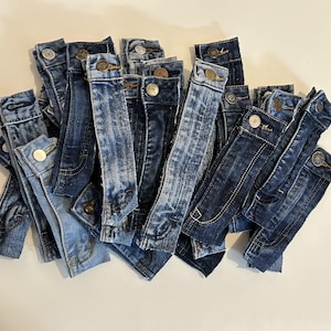 May include: A collection of denim fabric strips with metal buttons. The strips are various shades of blue and are arranged in a pile.