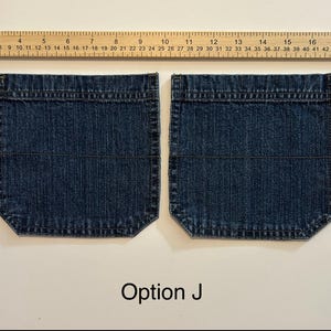 Pode incluir: Dois bolsos de ganga azul escuro com uma r&eacute;gua por cima. Os bolsos s&atilde;o retangulares com cantos arredondados e costuras horizontais. O texto "Op&ccedil;&atilde;o J" est&aacute; na parte inferior.