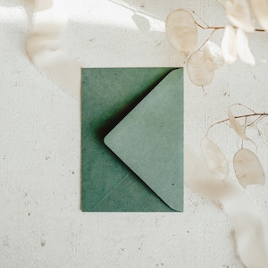 May include: A green envelope with a flap on a white textured surface. The envelope is made of textured paper.