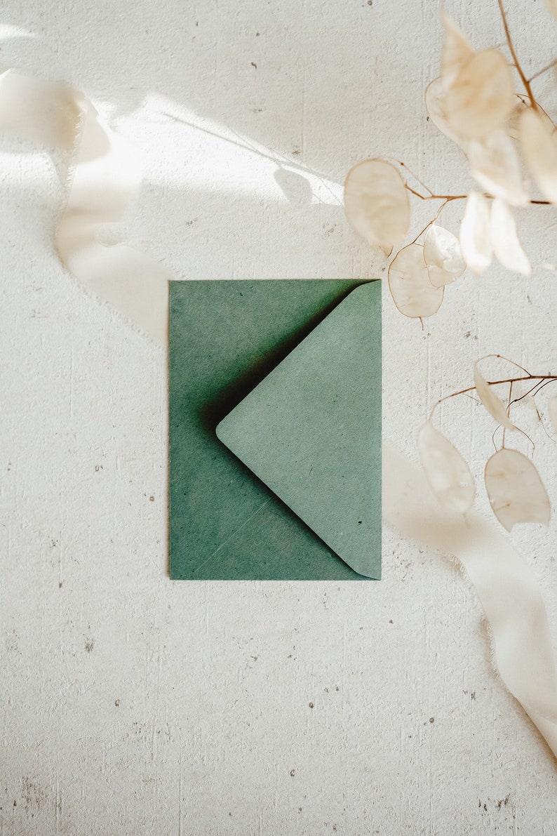 May include: A green envelope with a flap on a white textured surface. The envelope is made of textured paper.