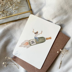 May include: A white card with a watercolor illustration of a person wearing a crown and riding a champagne bottle shaped like a rocket. The bottle is labeled with the number "40".