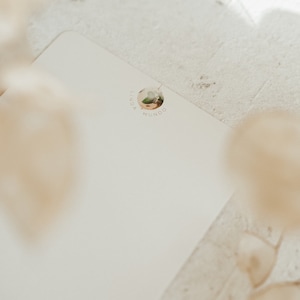May include: A white blank card with a round sticker featuring a floral design and the text "Linda Mundo".