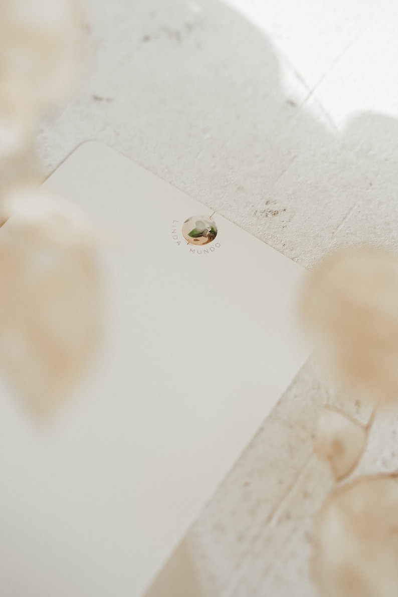 May include: A white blank card with a round sticker featuring a floral design and the text "Linda Mundo".