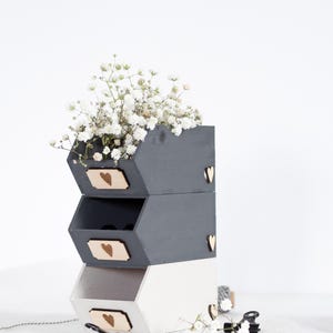 May include: Three-tiered wooden storage boxes, painted in grey and white, with heart-shaped details. The top box contains white flowers. Each box features a wooden label with a heart. Decorative and practical.