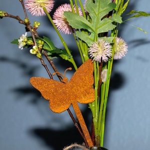 May include: A bouquet of pink flowers with green leaves and a rusty metal butterfly decoration.