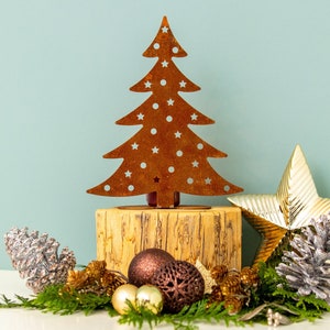 May include: A rustic metal Christmas tree cutout with white stars on a wooden base, surrounded by pine branches, gold and silver ornaments, and a gold star.