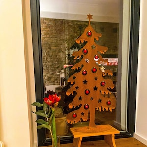 May include: A rustic metal Christmas tree with red ornaments and a star on top, standing on a wooden stool. A bowl of walnuts and a nutcracker are on the floor in front of the tree.