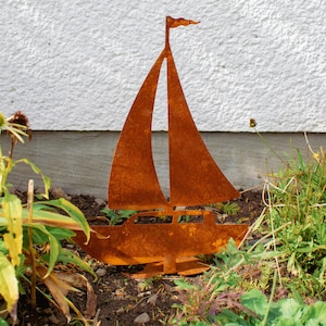 Könnte beinhalten: Eine rostige Metall-Segelschiffskulptur in einer Gartenlandschaft. Die Skulptur ist braun und orangefarben vor einem weißen Hintergrund.