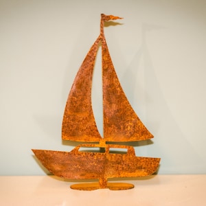 May include: A rusty metal sailboat sculpture with a sail and a small flag. The sculpture is standing on a white surface.