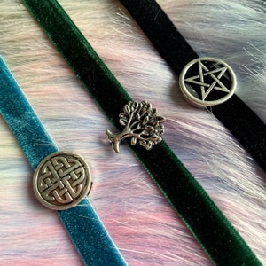May include: Three velvet choker necklaces with silver charms. The charms are a tree of life, a pentagram, and a Celtic knot. The necklaces are green, black, and blue.