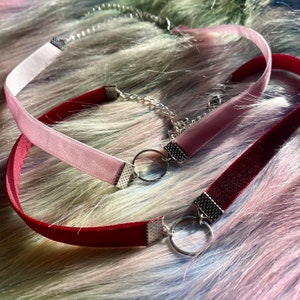 May include: Two velvet chokers with silver metal clasps and rings. One choker is pink and the other is burgundy.