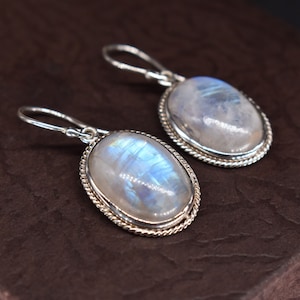 May include: A pair of silver earrings with oval-shaped moonstone gemstones. The earrings have a delicate, braided design around the edges of the stones.