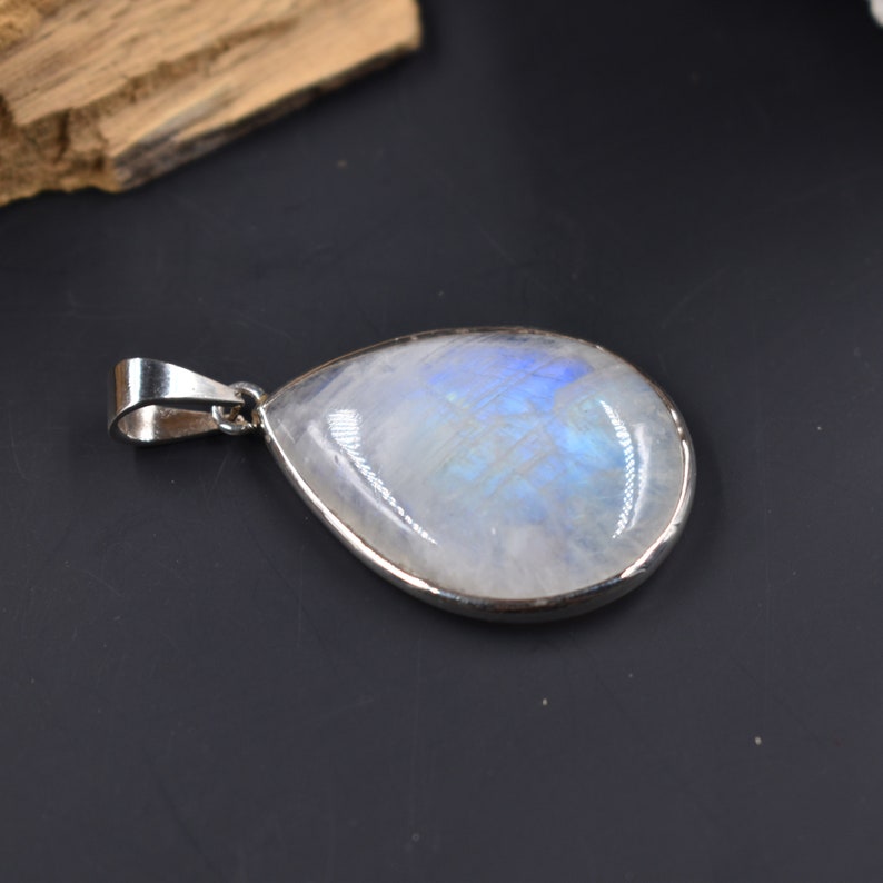 Pode incluir: Um pingente de pedra da lua em forma de l&aacute;grima com uma configura&ccedil;&atilde;o de prata. A pedra da lua tem uma cor branca leitosa com um brilho azul iridescente.