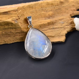 Pode incluir: Um pingente de pedra da lua em forma de l&aacute;grima com uma configura&ccedil;&atilde;o de prata. A pedra da lua &eacute; iridescente e tem um brilho azul.