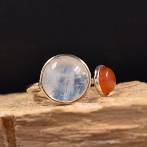 Pode incluir: Um anel de prata com uma pedra de lua branca e uma pedra de cornalina laranja.