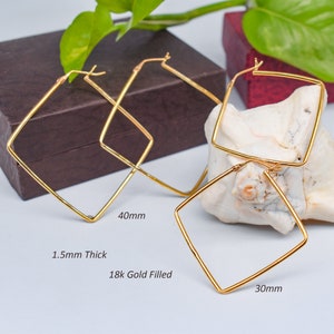 Peut inclure: Boucles d'oreilles créoles carrées en or. Les boucles d'oreilles mesurent 1,5 mm d'épaisseur et sont disponibles en tailles de 30 mm et 40 mm. Le texte sur l'image indique "18k Gold Filled".