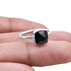 Peut inclure: Une bague en argent avec une pierre noire carrée et facettée. La bague a un fin anneau poli, et la pierre est sertie dans un sertissage carré. La bague est présentée sur un doigt.